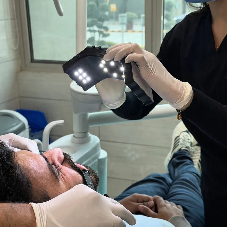 Dentist holding an LED dental photography light over a patient in the dental chair