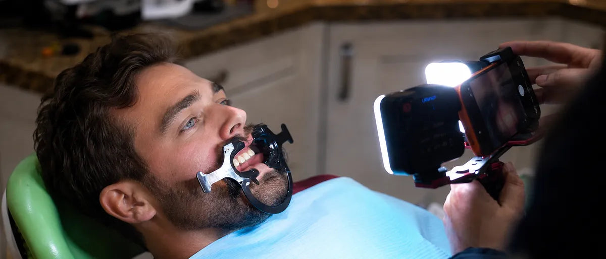 Dentist taking an intraoral photo with a smartphone and twin light while patient wears a retractor