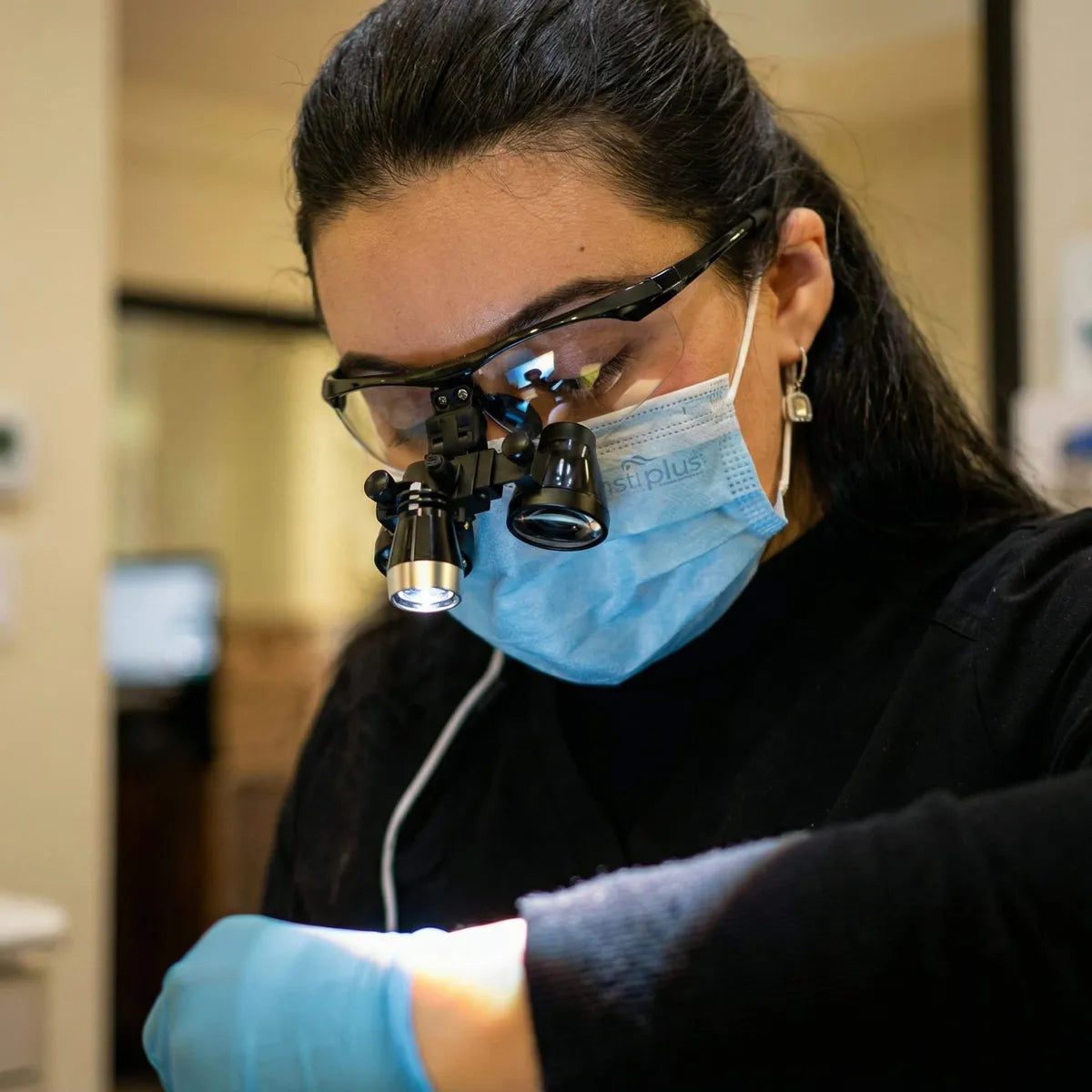Dentist wearing dental loupes with LED headlight during a procedure.